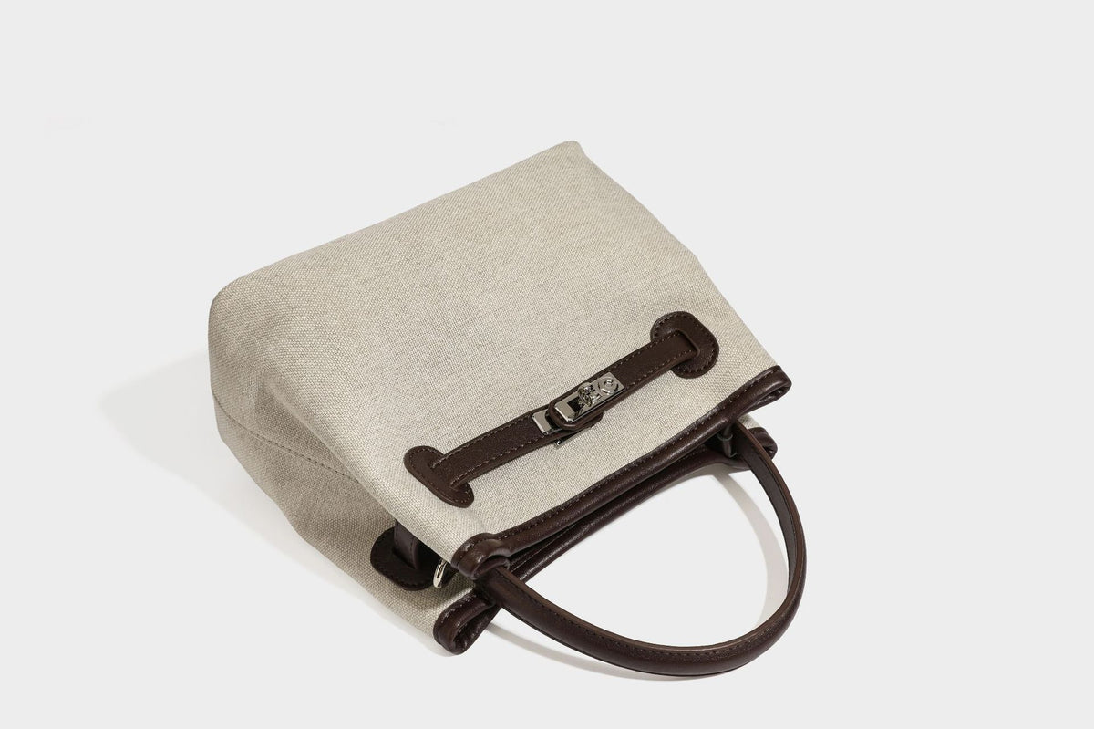 Small structured beige canvas top-handle bag with dark brown leather-look trim, silver turn-lock hardware, and detachable