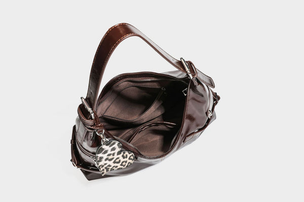 Glänzende dunkelbraune, lässig geschnittene Hobo-Schultertasche mit Riemendetail mit silberfarbenen Ösen, Reißverschlussfach auf der Vorderseite und Herz mit Leopardenmuster