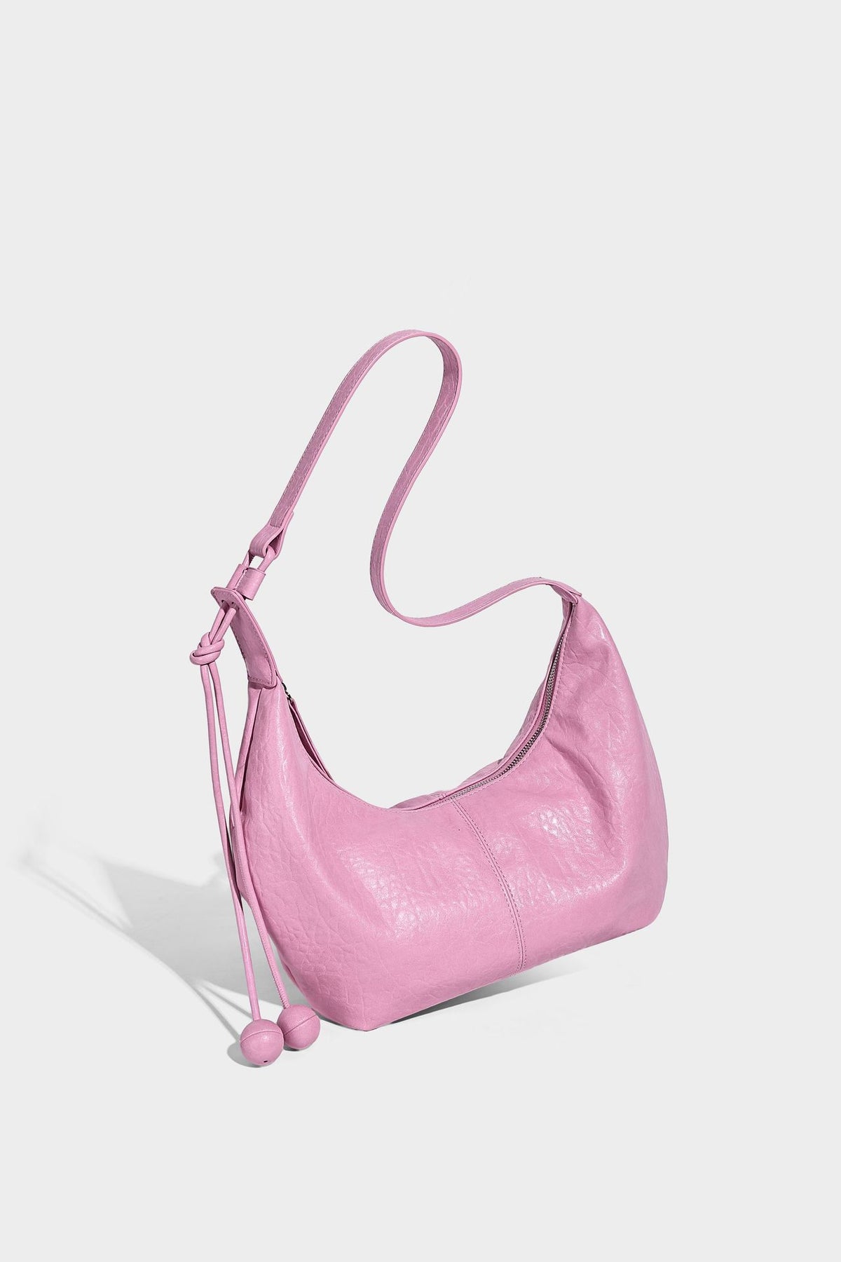Slouchy crescent half-moon shoulder bag in pink pebbled textured finish with floral charm and knotted side detail, detail