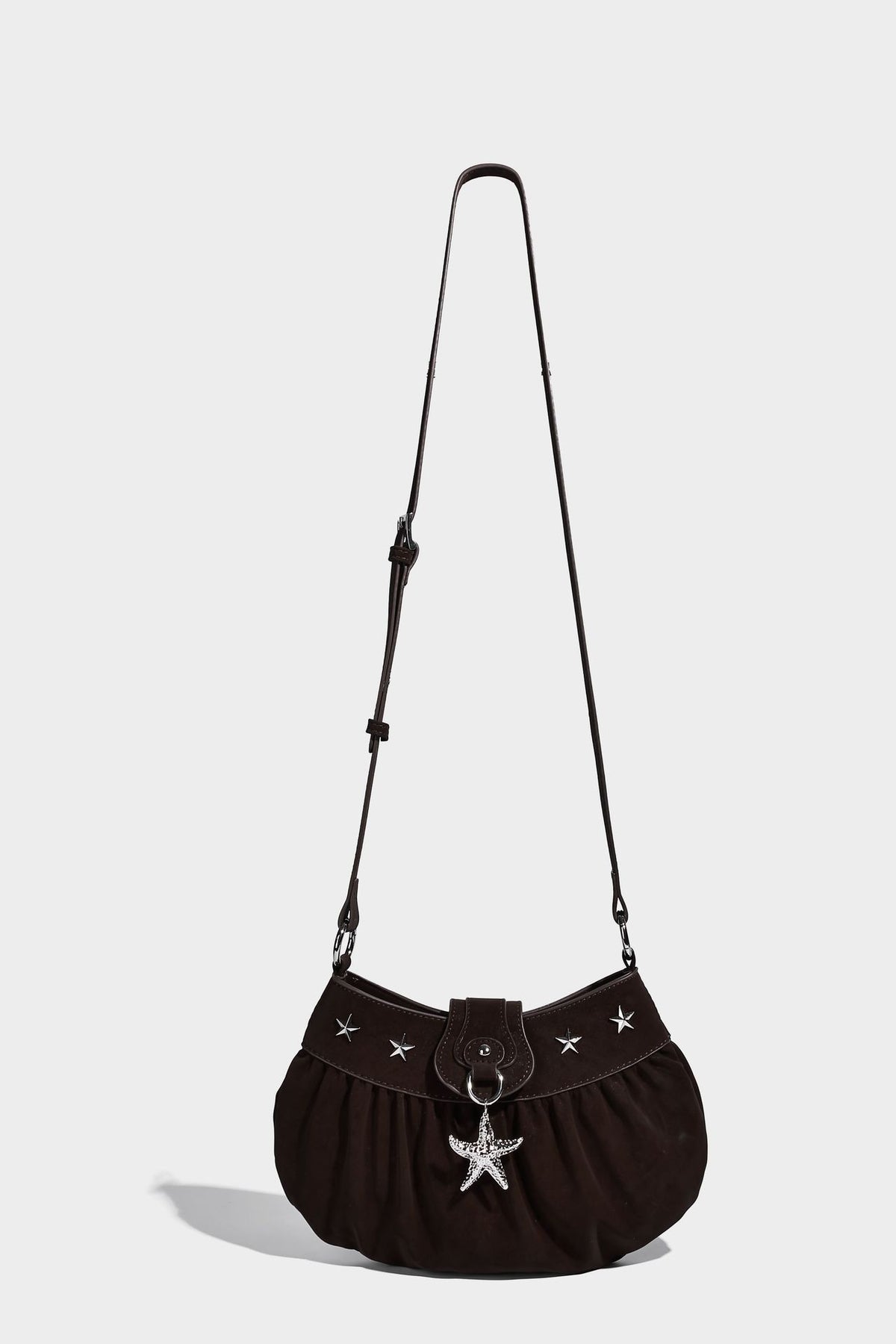 Ruched shoulder bag with curved flap, silver star studs, dangling starfish charm, and adjustable crossbody strap, detail view