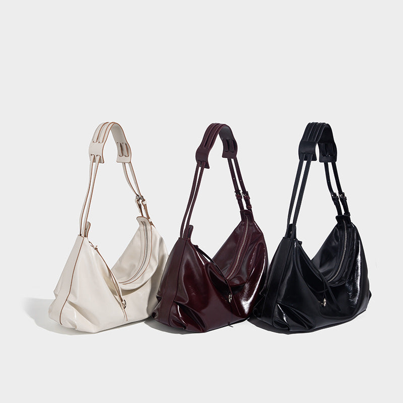 Glossy black slouchy hobo shoulder bag with zip closure, silver-tone ring hardware, and adjustable crossbody strap, detail