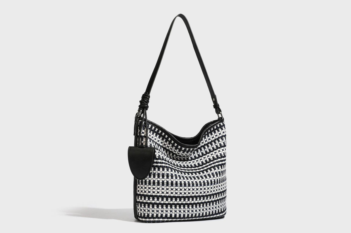 Woven stripe bucket shoulder bag in cream and dark brown with leather-look trim, knotted adjustable strap, and small shield