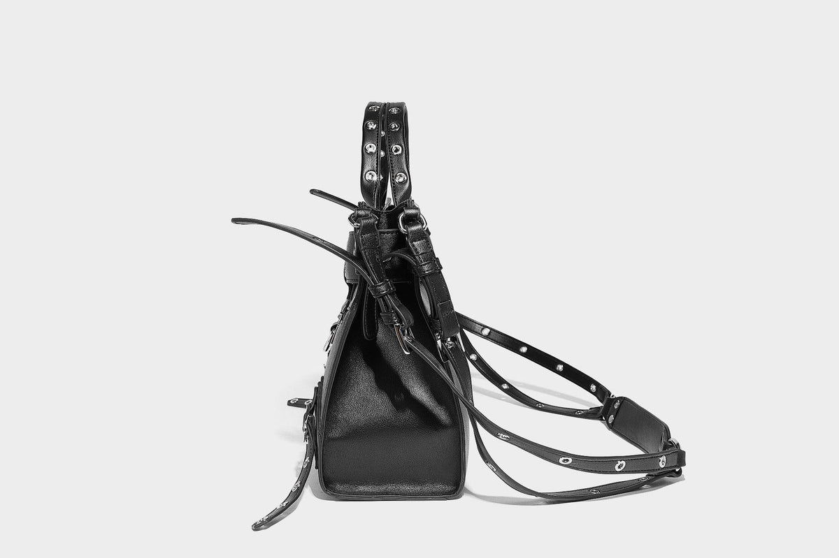 Black structured rectangular satchel bag with silver-tone rivets, large front buckle strap, zip pockets, dual top handles