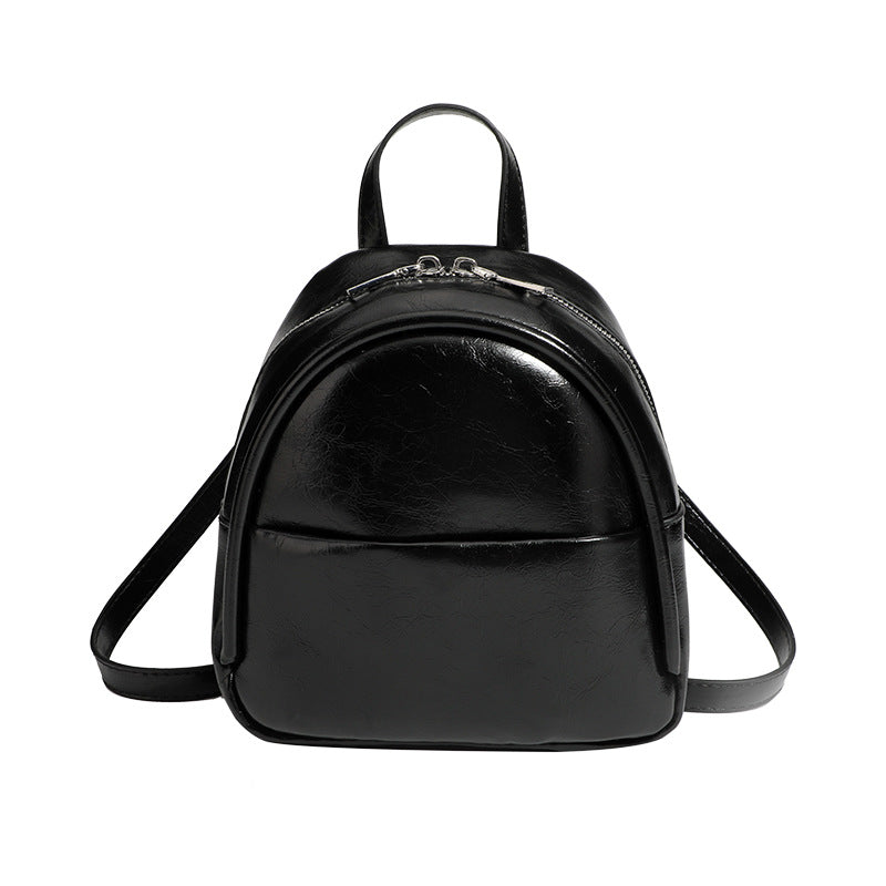 Kompakter, abgerundeter Mini-Rucksack im Lederlook mit glänzender Oberfläche, Reißverschluss oben, Vordertasche und Tragegriff oben, Detailansicht