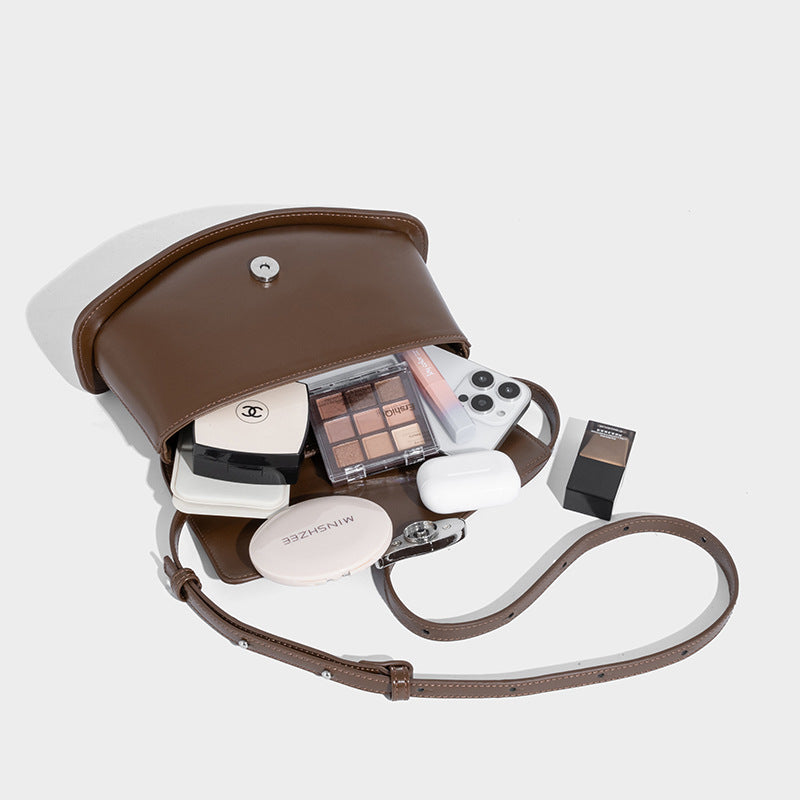 Small structured saddle bag with glossy leather-look finish, angular flap front, silver-tone metal clasp, and slim