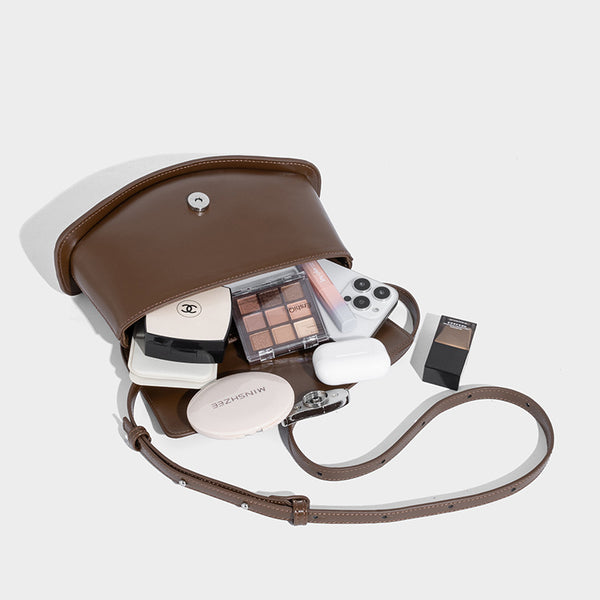 Small structured saddle bag with glossy leather-look finish, angular flap front, silver-tone metal clasp, and slim