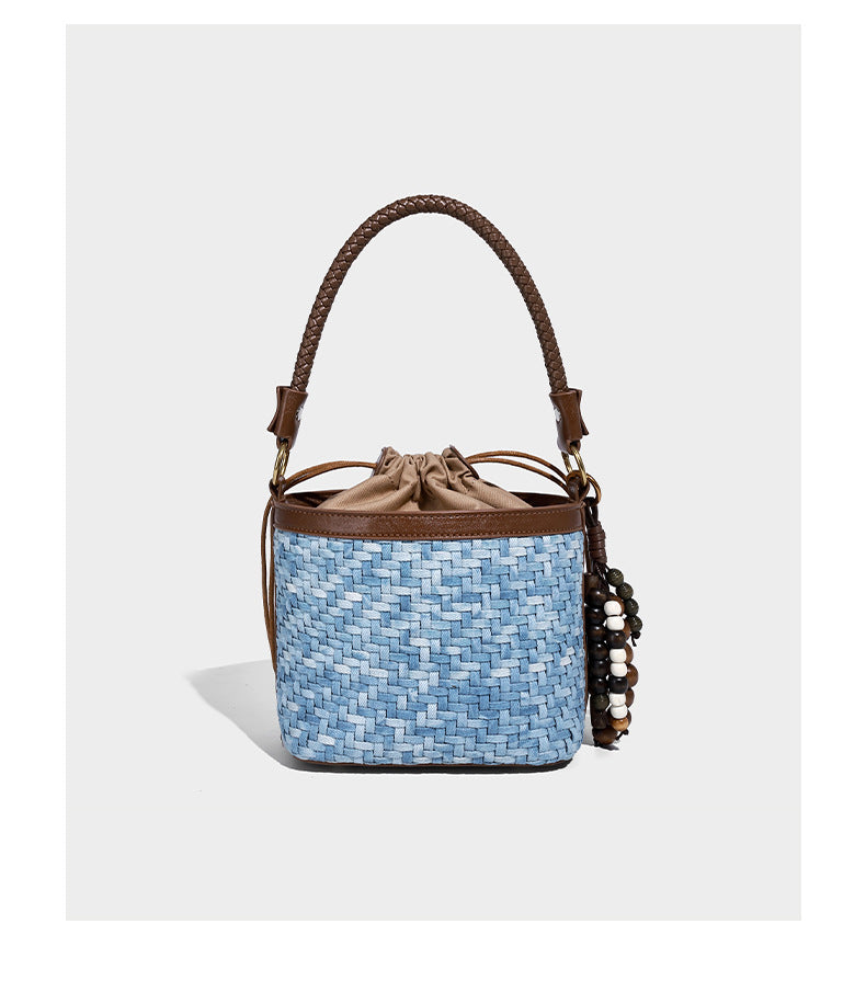 Small light blue woven bucket bag with brown leather-look trim, braided top handle, brass-tone ring hardware, drawstring