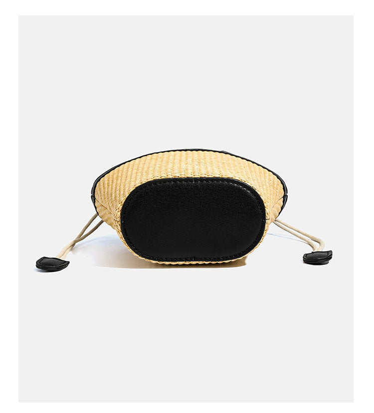 Kleine geflochtene Bucket Bag aus Stroh mit schwarzem Besatz in Lederoptik, zwei oberen Tragegriffen, cremefarbenem Futter mit Kordelzug und seitlichen Kordelverschlüssen