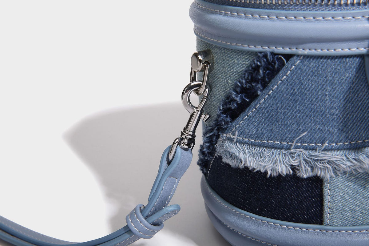 Mini cylindrical barrel bucket bag in denim patchwork with frayed edges, smooth leather-look trim, zip-around top closure