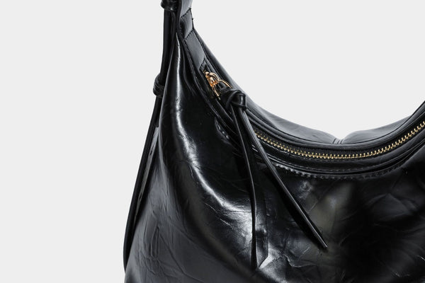 Übergroße, lässig fallende Hobo-Schultertasche aus glänzendem, geknittertem Lederimitat mit goldfarbenem Reißverschluss und Emblem-Beschlägen, Detailansicht