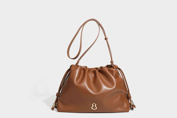 Slouchy ruched drawstring shoulder bag in smooth leather-look finish with gold-tone emblem and slim adjustable strap, detail