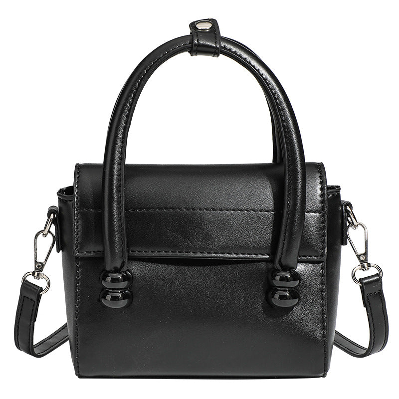 Kleine strukturierte schwarze Henkeltasche im Lederlook mit zwei abgerundeten Henkeln, abnehmbarem Umhängeriemen und silberfarbenem