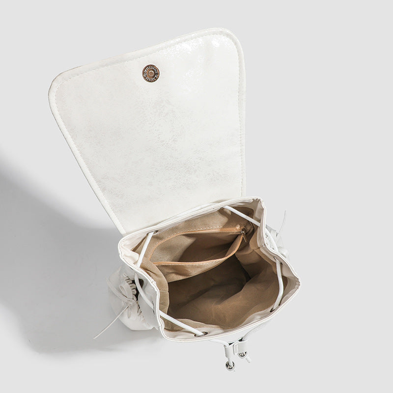 Compact white pearlescent flap backpack with silver-tone bow hardware and drawstring closure, detail view 4