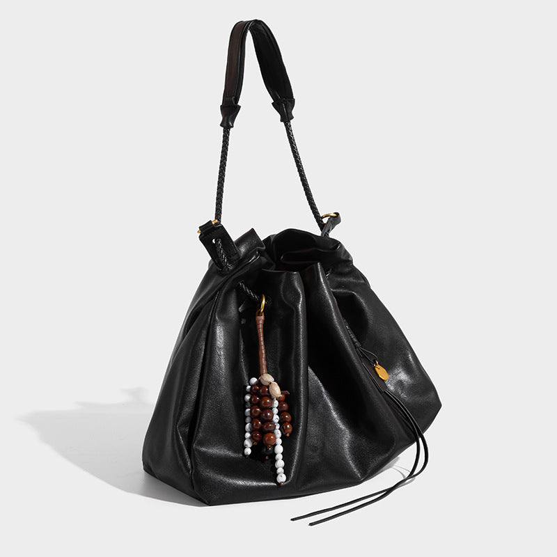 Cream slouchy drawstring bucket bag with braided cord, beaded tassel charm, and gold-tone ring hardware, detail view 3