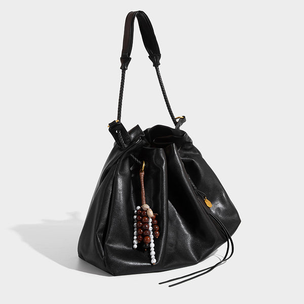 Cream slouchy drawstring bucket bag with braided cord, beaded tassel charm, and gold-tone ring hardware, detail view 3