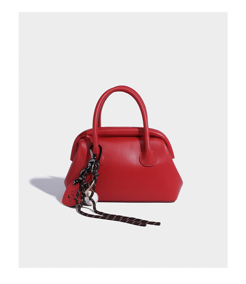 Small structured shell top-handle bag in red with heart charm and braided cord detail, smooth leather-look finish, detail