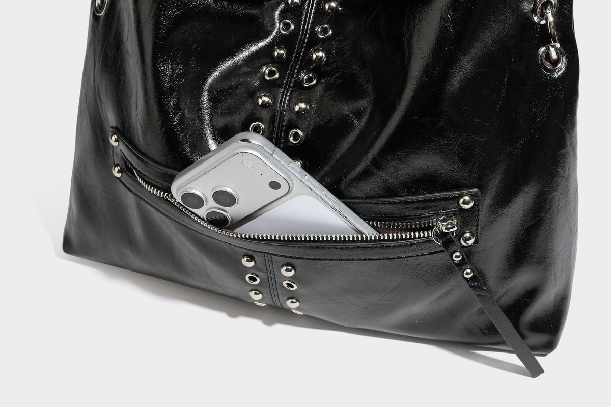 Black glossy leather-look slouchy shoulder bag with silver stud and eyelet hardware, top zip closure, front zip pocket, and