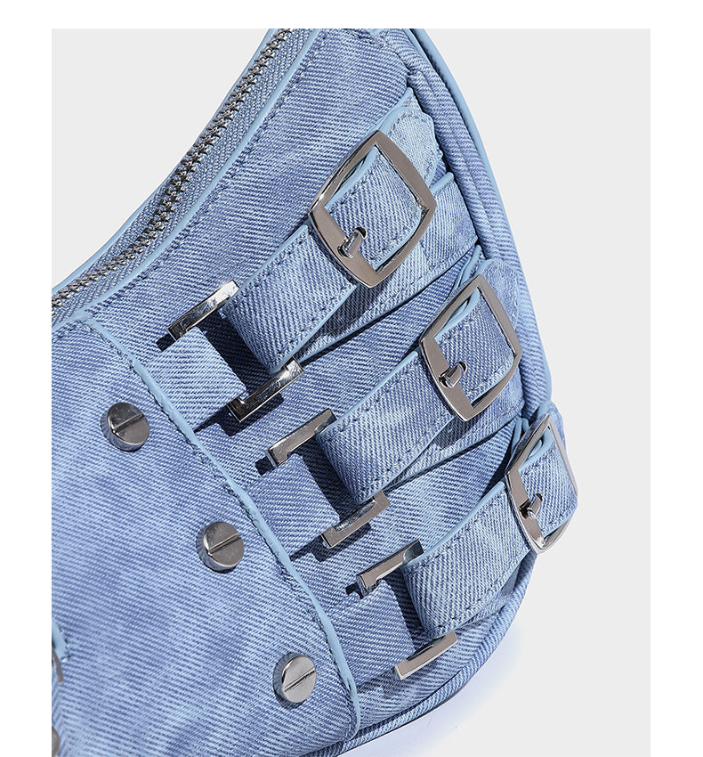 Crescent shoulder bag in washed blue denim-look PU with stacked buckle straps, front zip pocket, and silver-tone hardware