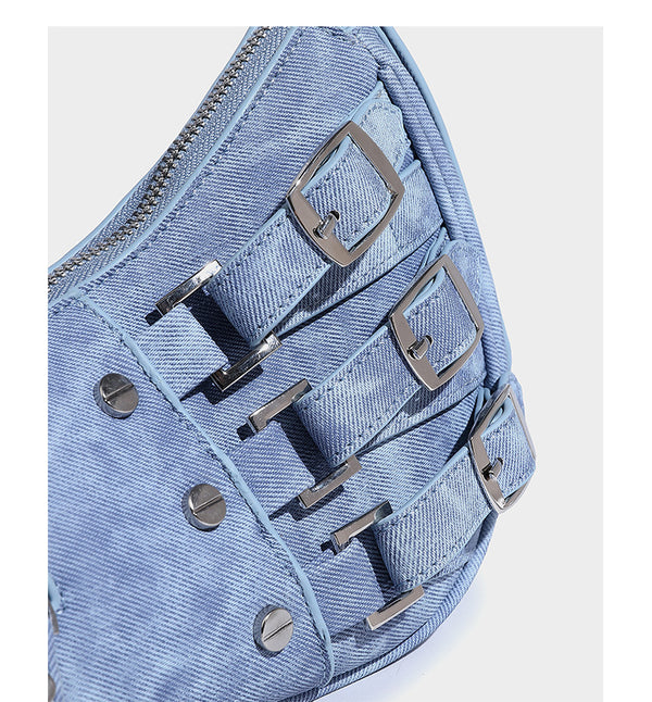 Crescent shoulder bag in washed blue denim-look PU with stacked buckle straps, front zip pocket, and silver-tone hardware