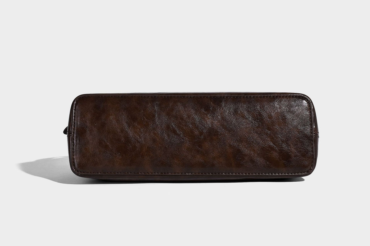 Strukturierte dunkelbraune Henkeltasche mit Öl-Wachs-Finish, vorderer Gürtelschnalle, goldfarbenen Beschlägen und zwei Tragegriffen, Detailansicht