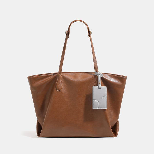 Large soft trapezoid tote bag with leather-look finish, dual shoulder straps, and gray hanging card tag, detail view 7