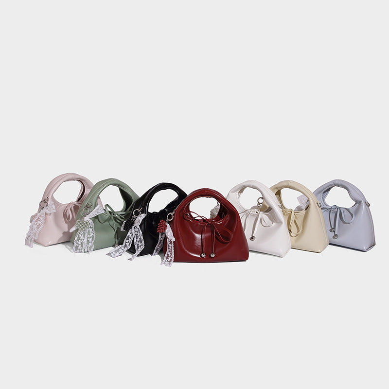 Small glossy leather-look dome top-handle bag with drawstring tie closure, white lace bow charm, and silver-tone hardware