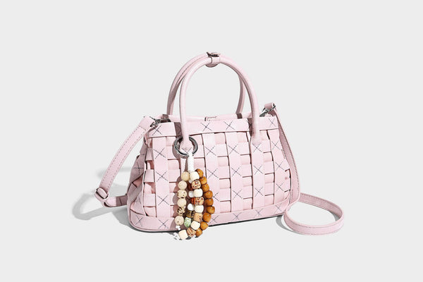 Small structured woven satchel tote with rounded top handles, silver-tone ring hardware, and bead tassel charm, detail view