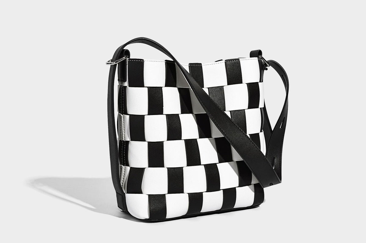 Hand-woven black-and-white checkerboard bucket bag with smooth black trim, silver-tone ring hardware, and adjustable