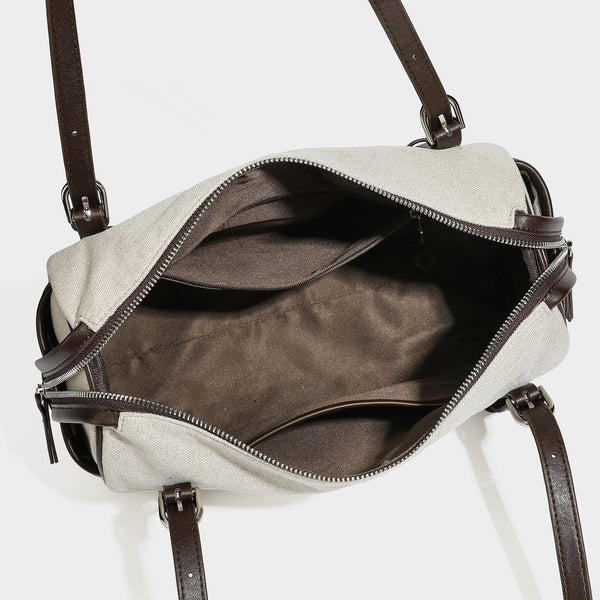 Beige canvas barrel bag with dark brown leather-look trim, silver-tone hardware, top zip closure, and adjustable shoulder