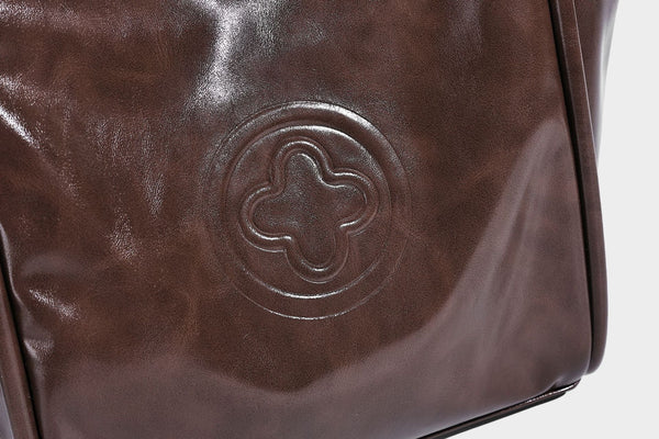 Glossy leather-look structured tote bag with rounded top handles, detachable shoulder strap, embossed front emblem, and side