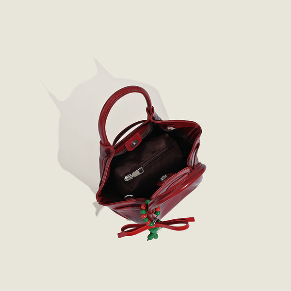 Small structured red glossy PU handbag with bow-and-bead charm, dual top handles, and detachable crossbody strap, detail view