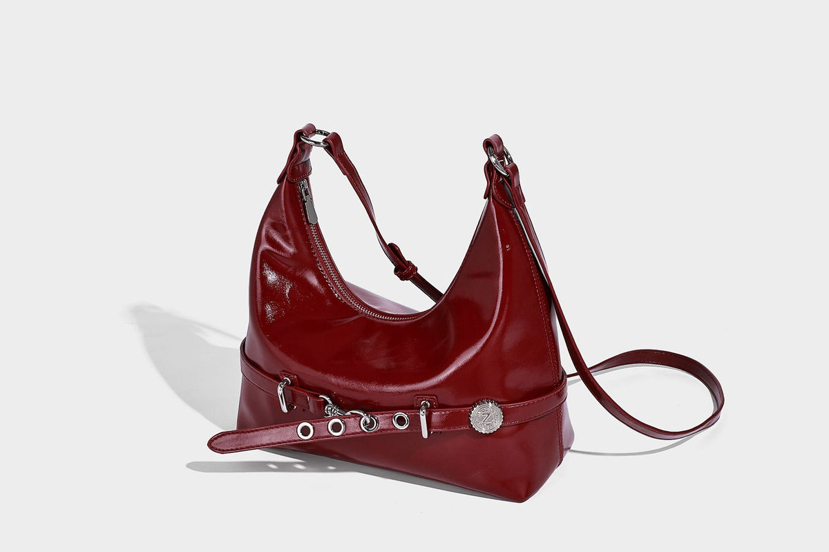 Glossy black slouchy hobo shoulder bag with silver-tone hardware, belt-style grommet strap at base, and long adjustable