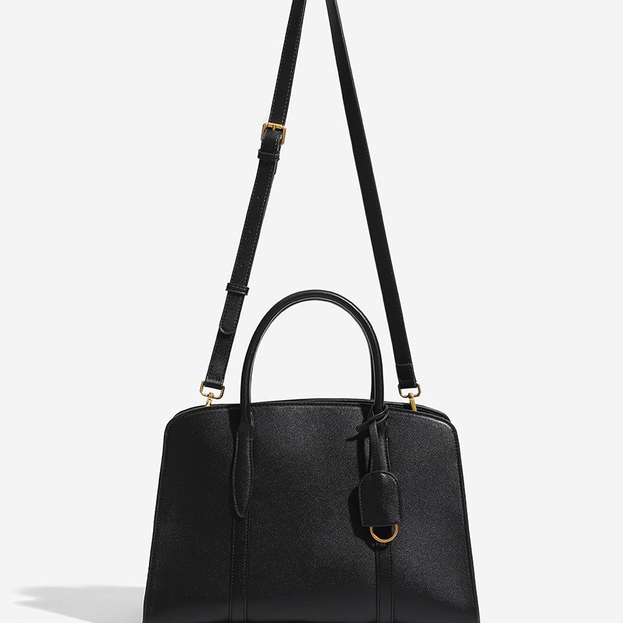 Structured trapezoid Boston satchel bag with dual top handles, gold-tone lock charm, and top zip closure, detail view 2