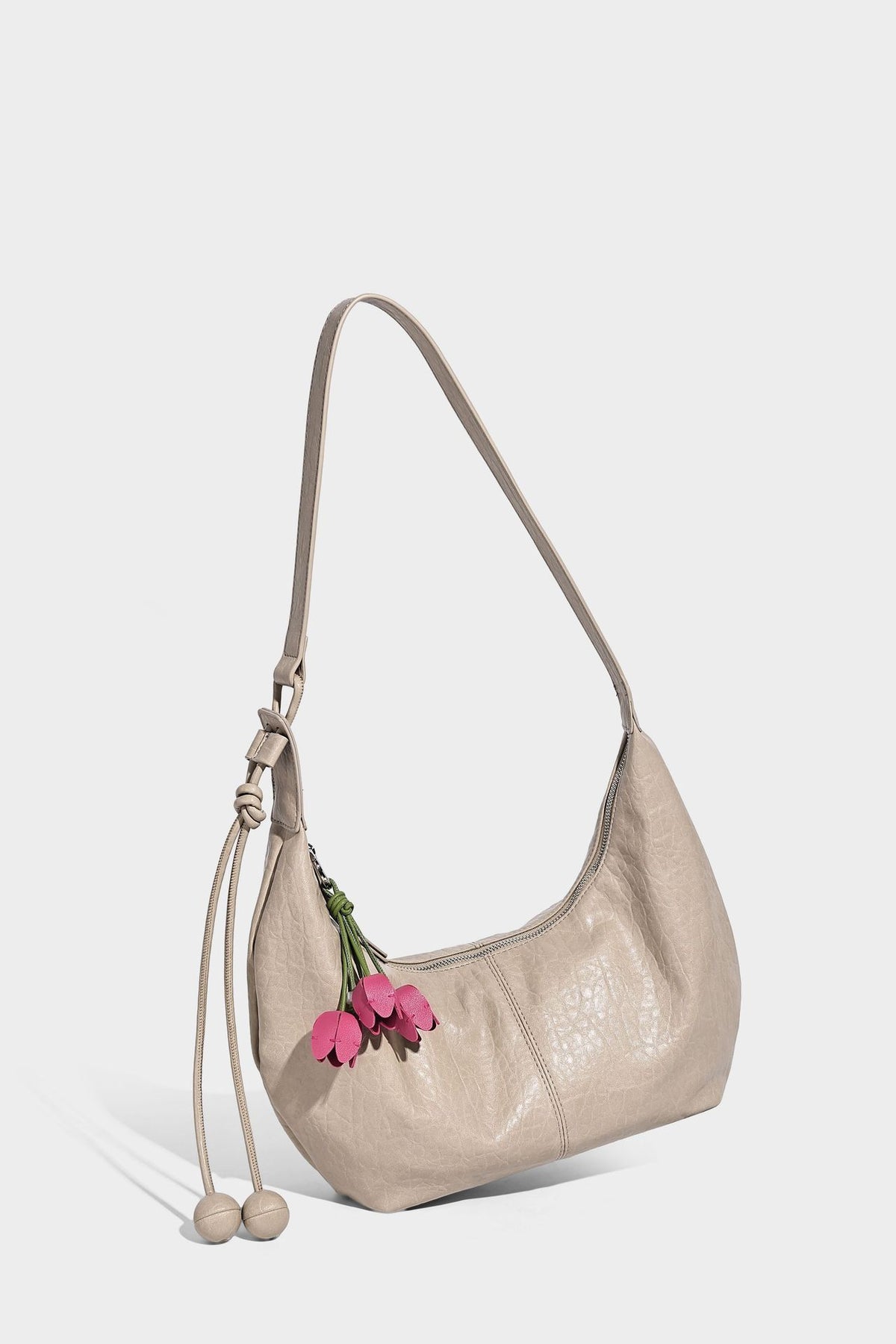 Slouchy crescent half-moon shoulder bag in pink pebbled textured finish with floral charm and knotted side detail, detail