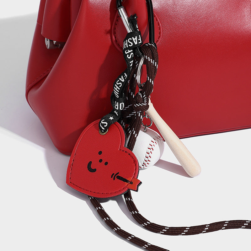 Small structured shell top-handle bag in red with heart charm and braided cord detail, smooth leather-look finish, detail