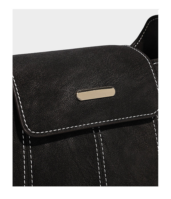 Small matte textured bucket crossbody bag with flap closure, gold-tone bar hardware, contrast stitching, and pompom tassel