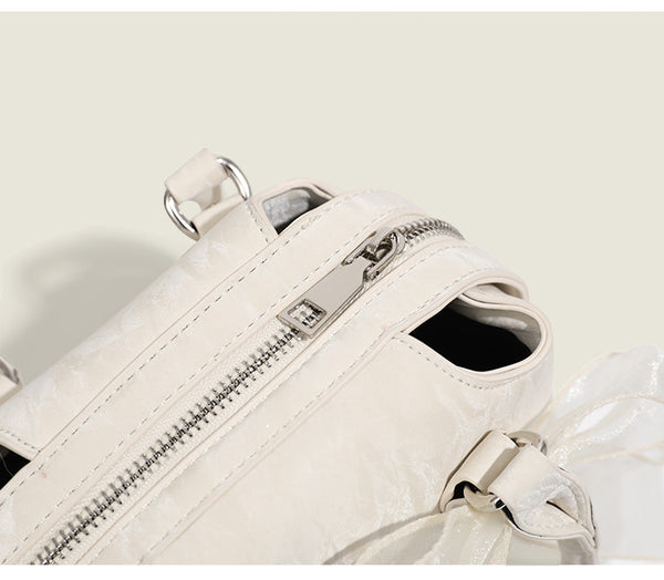 Small structured Boston bag in cream with glossy crinkled finish, sheer bow accent, silver-tone hardware, dual top handles
