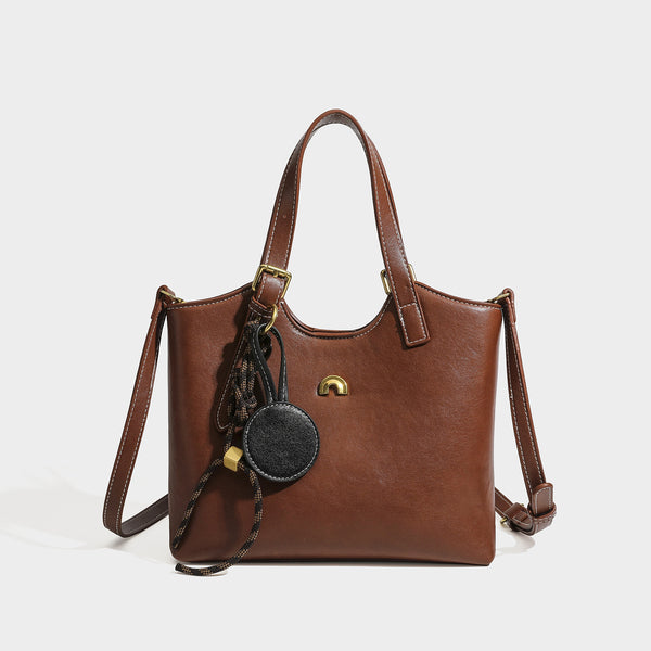 Structured smooth leather-look tote bag with long shoulder strap, gold-tone hardware, and hanging tassel-coin charm, front