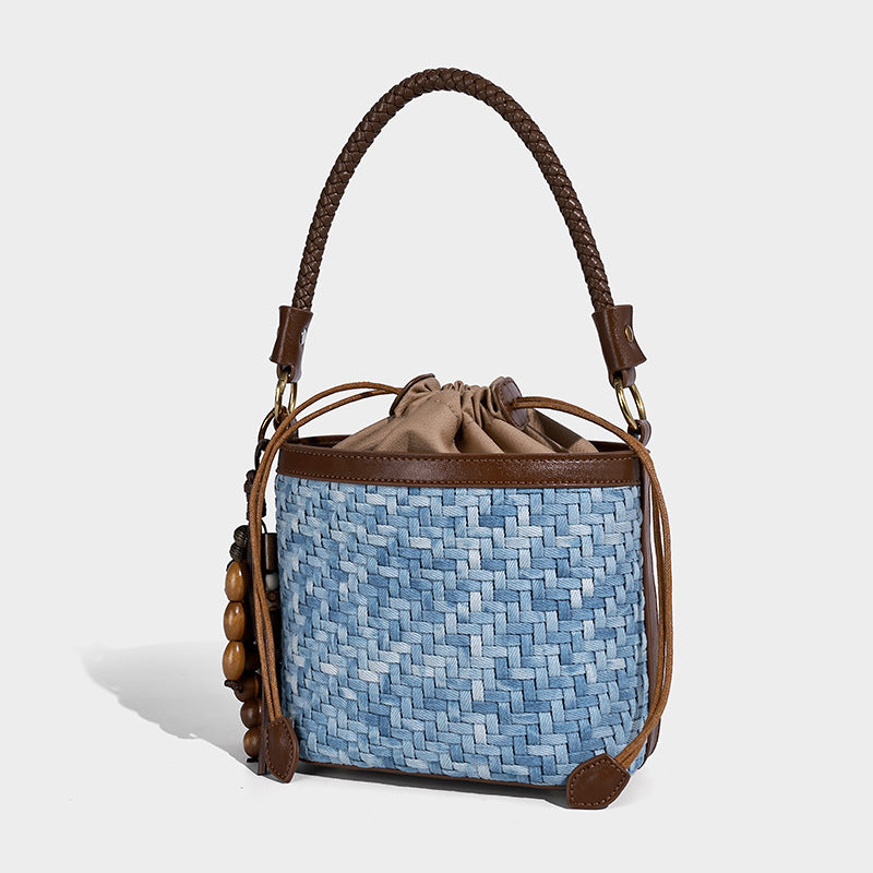 Small light blue woven bucket bag with brown leather-look trim, braided top handle, brass-tone ring hardware, drawstring