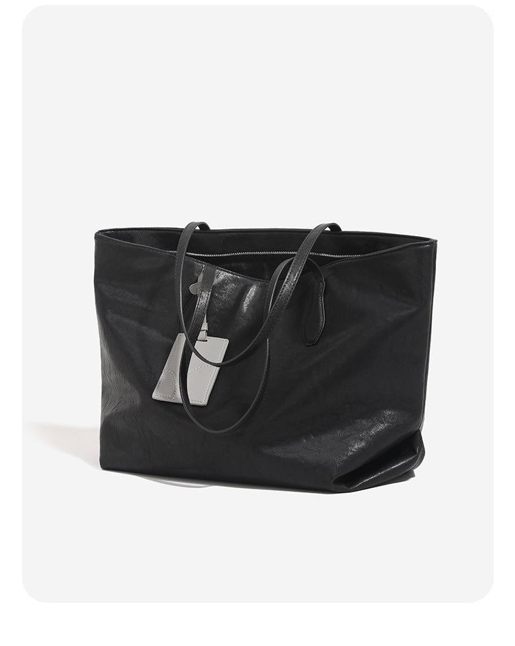 Oversized slouchy leather-look tote bag with long shoulder straps, contrast grey hanging tag, and silver-tone hardware