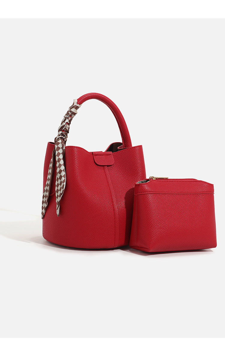 Pebbled leather-look bucket bag with checkered scarf-wrapped top handle, flap tab closure, gold-tone hardware, and matching