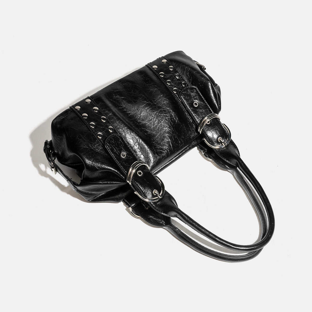 Compact black glossy leather-look satchel bag with silver-tone rivets, buckle hardware, and dual padded top handles, detail