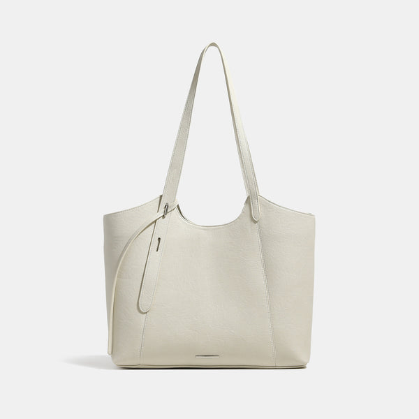 Structured trapezoidal tote bag with smooth leather-look finish, long black contrast shoulder straps, and dangling strap