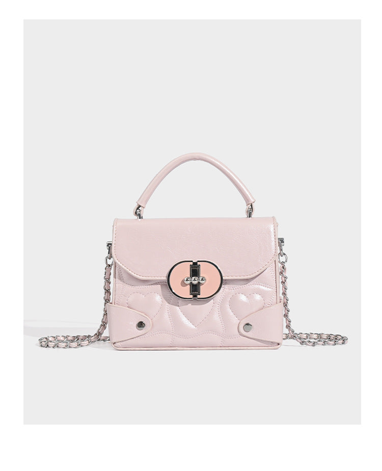 Kleine strukturierte Box-Tasche aus herzförmig gestepptem PU mit Henkel, silberfarbenem Kettenriemen zum Tragen als Crossbody und ovalem Drehverschluss, Detailansicht