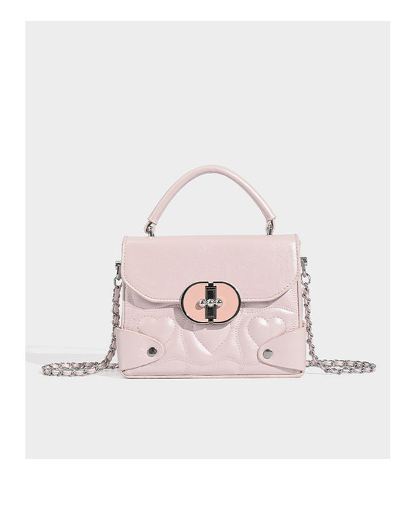 Kleine strukturierte Box-Tasche aus herzförmig gestepptem PU mit Henkel, silberfarbenem Kettenriemen zum Tragen als Crossbody und ovalem Drehverschluss, Detailansicht