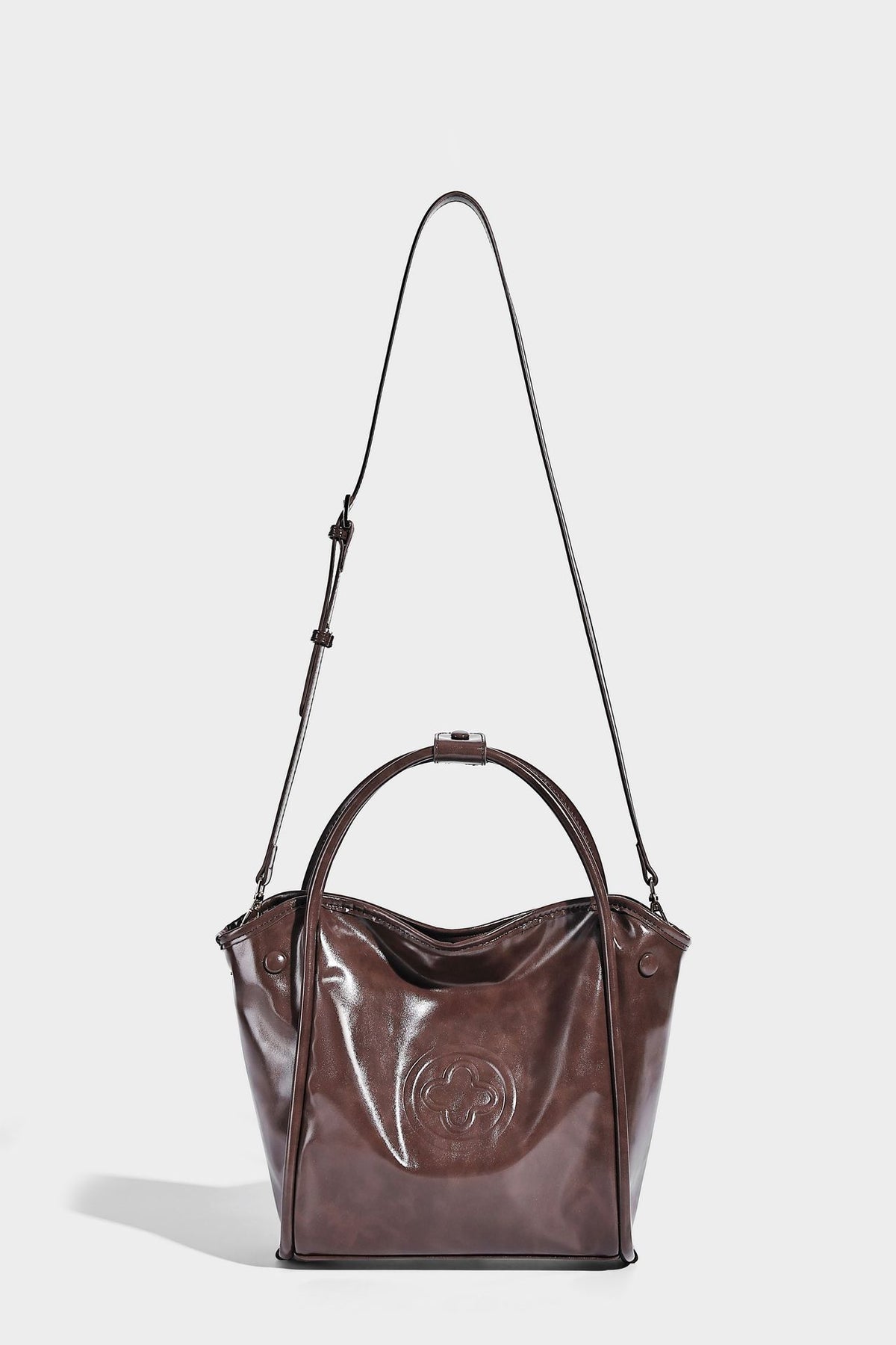 Glossy leather-look structured tote bag with rounded top handles, detachable shoulder strap, embossed front emblem, and side