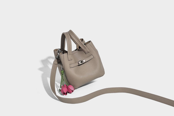 Small structured pebbled bucket tote bag with dual top handles, silver turn-lock front pocket, and detachable shoulder strap