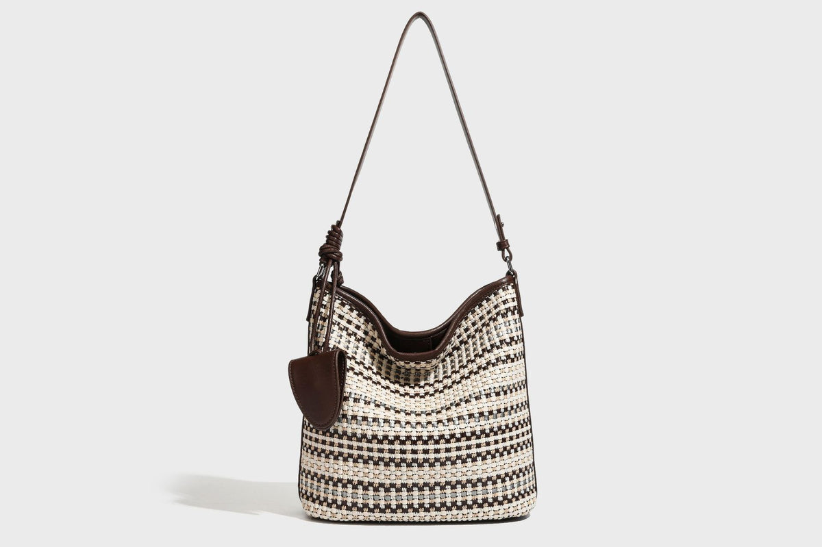 Woven stripe bucket shoulder bag in cream and dark brown with leather-look trim, knotted adjustable strap, and small shield