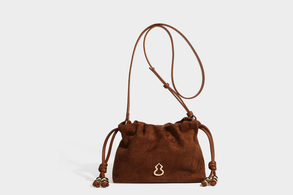 Suede-look drawstring shoulder bag in brown with smooth trim, knotted bead drawstring closure, slim adjustable strap, and