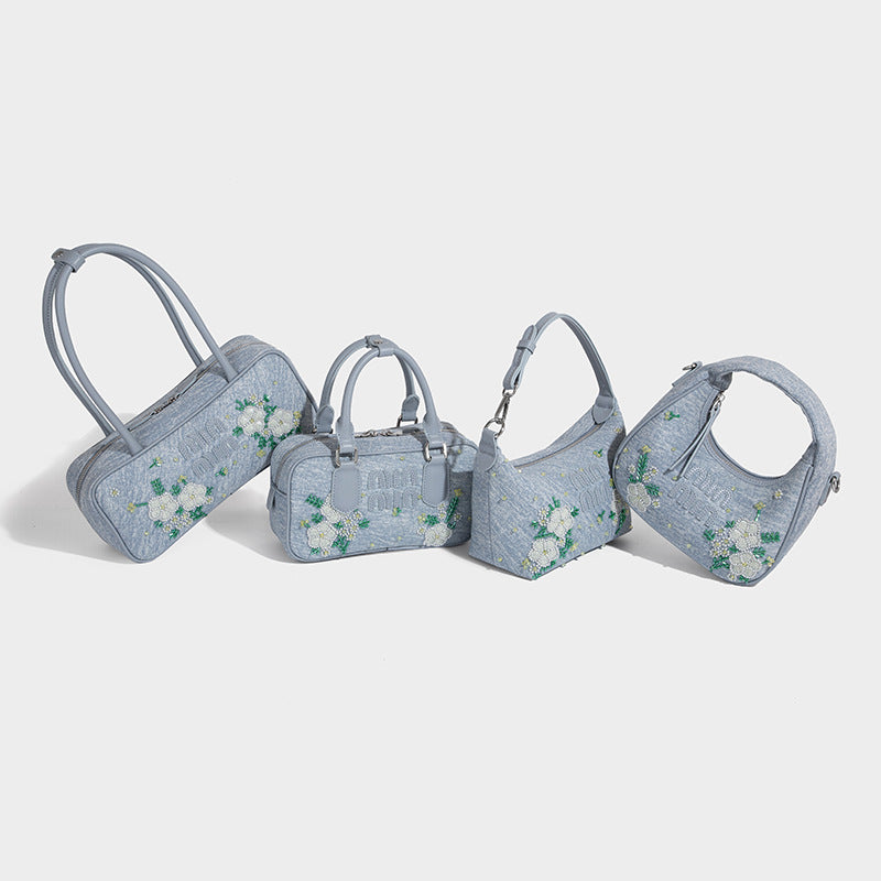 Small light blue denim-look barrel bag with white floral bead embroidery, dual top handles, and detachable shoulder strap